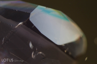 Twin plane at one end of an unusual synthetic pink sapphire with artificial orange stains and dendrite patterned in induced fissures. Fine needles were seen along this twin plane and could easily cause a gemologist to reach the conclusion that the stone was natural.