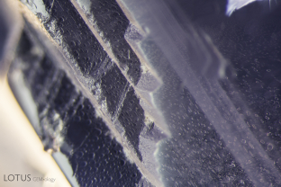 Etch marks of the surface of a natural (in the left portion of the photo), along with a fingerprint inclusion within the gem itself (right side of the photo). Note the identical pattern of the etch marks and the negative crystals within the fingerprint, both reflections of the underlying atomic symmetry.