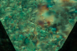 Irregularities in the crystal structure create the roiled “gota de aceite,” (Spanish for “drop of oil”) effect in this emerald. This effect is often associated with Colombian emeralds. Here crossed polars reveal strain patterns between the growth structures.